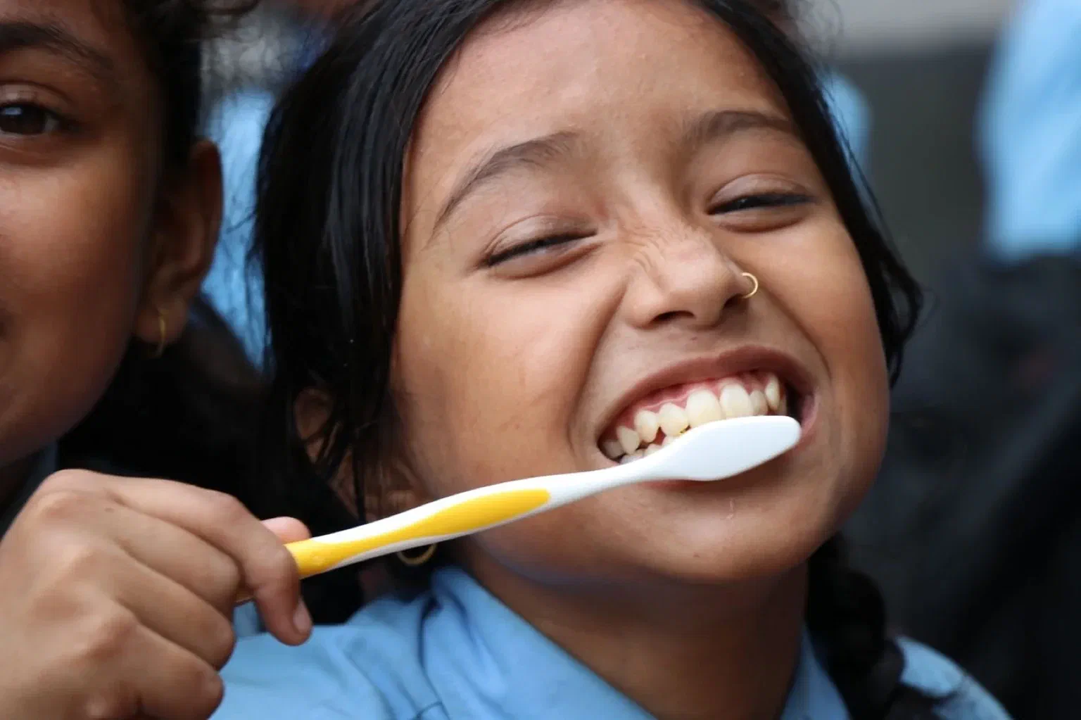 A smiling child brushes her front teeth with a yellow toothbrush