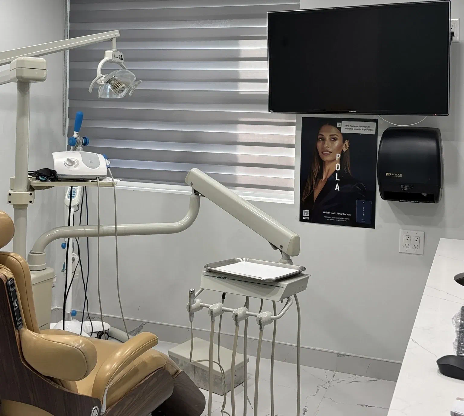 A treatment room at Milton Dental Clinic with a dental chair, examination light, and wall-mounted screen