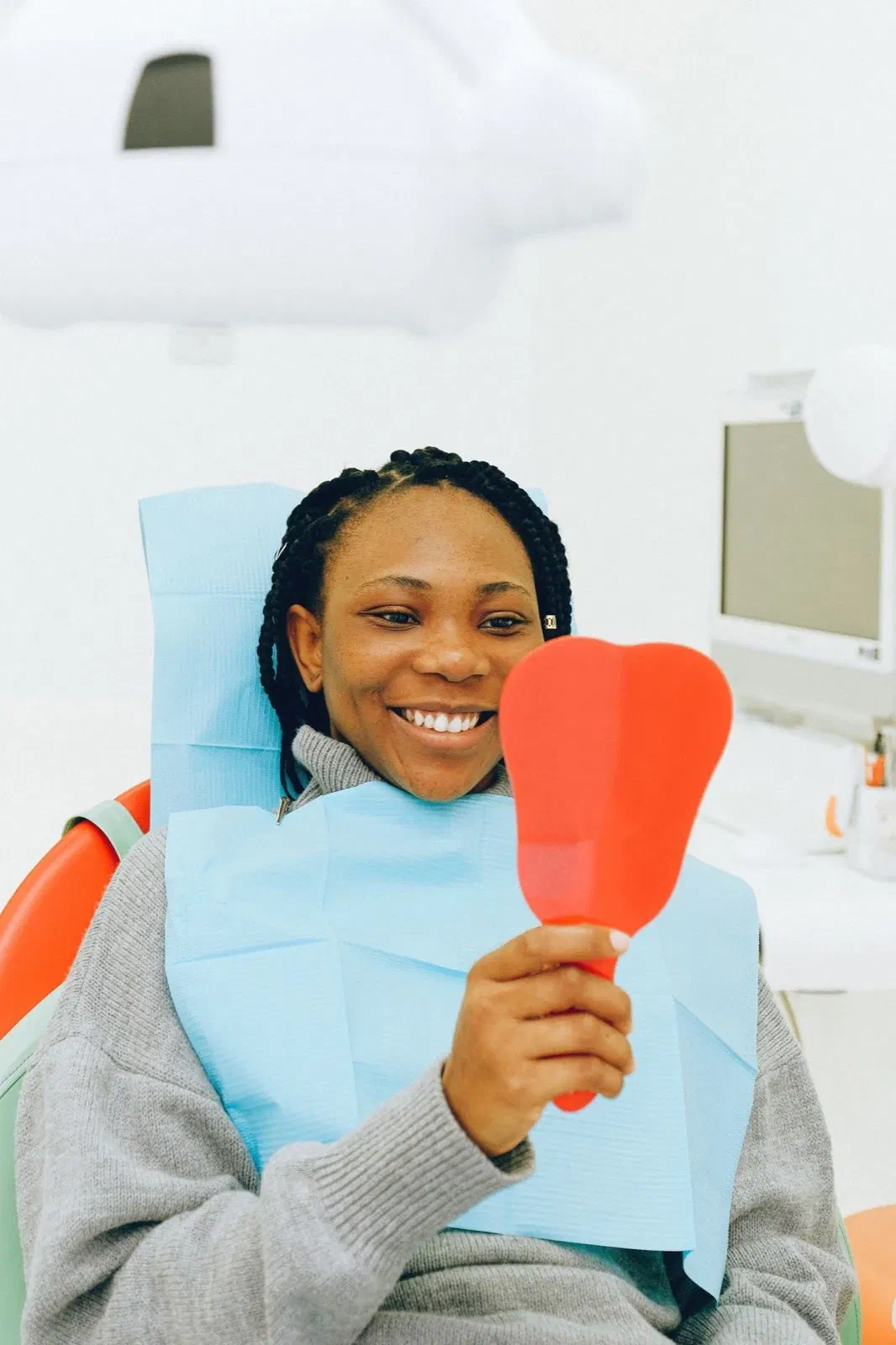 A patient smiles while looking into a handheld mirror in a dental chair