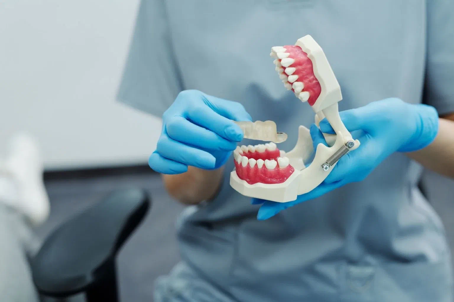 A gloved dental professional demonstrates replacement teeth on a hinged jaw model